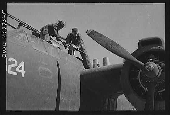 An American plane mechanic assisted by an Iranian boy working on a light bomber before delivery to Russia. Somewhere in Iran.