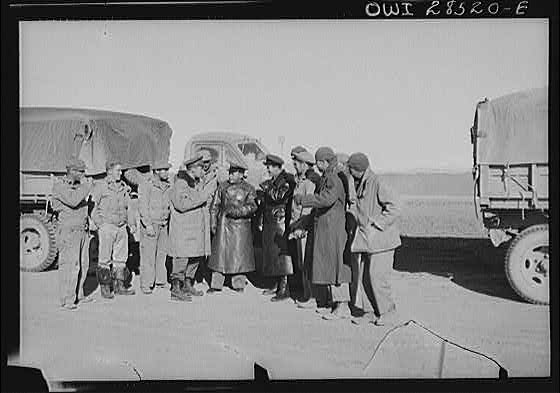 Russian officers in black leather coats surrounded by a group of American soldiers, truck drivers at a dumping spot for supplies which the Americans brought through the Persian corridor. This was one of the first all-American convoys to make the trip bringing aid to Russia. Somewhere in Iran.